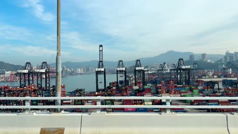 Tagsüber-Vorbeifahrt-Am-Geschäftigen-Hongkonger-Schifffahrtshafen-Mit-Portalkränen-Und-Zahlreichen-Containern