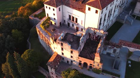 Aerial-view-over-a-medieval-castle-on-top-of-a-hill,-surrounded-by-prosecco-vineyards,-in-Italy,-at-sunrise