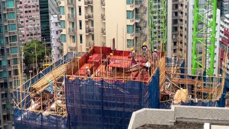 Bauarbeiter-In-Hongkong-Arbeiten-Auf-Dem-Dach-Eines-Neu-Errichteten-Hochhauses,-Das-Von-Bambusgerüsten-Umgeben-Ist