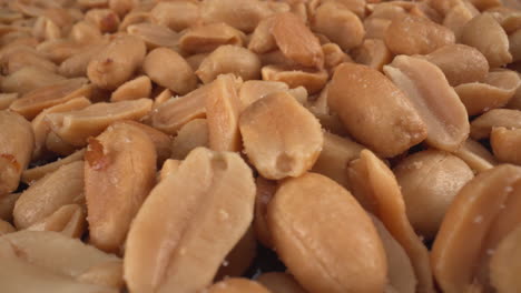 Salted-toasted-peanuts-turning-macro-view,-food-product-used-in-many-commercial-producers-and-recipes-like-chocolates,-sauces-and-oils,-known-allergen,-healthy-nuts,-peanut-allergy,-4K-shot