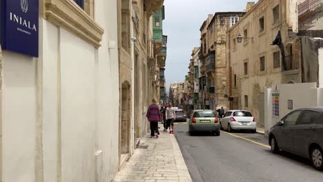 Menschen,-Die-Auf-Dem-Bürgersteig-Gehen,-Während-Ein-Auto-An-Einem-Sonnigen-Tag-In-Valletta-Auf-Einer-Engen-Straße-Vorbeifährt