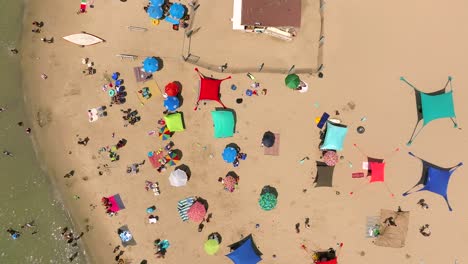 Summer-day-at-the-beach-with-people-in-the-water-and-under-colorful-umbrellas,-Top-down-drone-footage