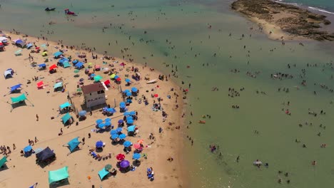 Summer-day-at-the-beach-with-people-in-the-water-and-under-colorful-umbrellas,-Top-down-drone-footage