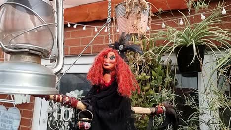 Magical-red-haired-handmade-witch-on-broomstick-hanging-with-lantern-and-plants-in-home-garden-sanctuary