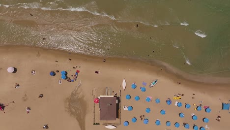 Día-De-Verano-En-La-Playa-Con-Gente-En-El-Agua-Y-Bajo-Sombrillas-Coloridas,-Imágenes-De-Drones-De-Arriba-Hacia-Abajo