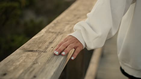 Painted-nails-woman's-hand-caressing-a-wooden-handrail-walkway