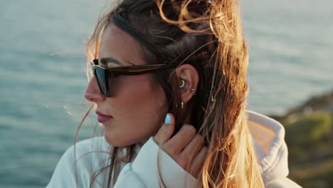 Close-up-portrait-of-woman-wearing-sunglasses-tucks-her-hair-behind-the-ear-with-hand