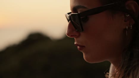 Close-up-of-the-face-of-a-young-woman-wearing-sunglasses-eating-a-sweet-at-sunset