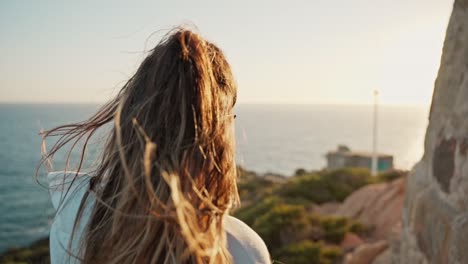Young-woman-watching-the-sunset-on-the-sea-while-the-wind-sways-her-hair-with-highlights