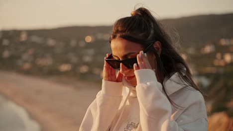 Beautiful-young-model-woman-with-hoodie,-sunglasses-poses-for-the-camera-in-the-golden-sunlight-during-the-sunset-dawn