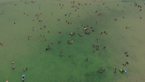 Sommertag-Am-Strand-Mit-Menschen-Im-Wasser-Und-Unter-Bunten-Sonnenschirmen,-Drohnenaufnahmen-Von-Oben-Nach-Unten