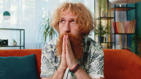 Worried-Caucasian-redhead-man-praying-sincerely-with-folded-arms-asking-God-for-help-begging-apology