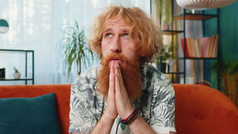 Worried-Caucasian-redhead-man-praying-sincerely-with-folded-arms-asking-God-for-help-begging-apology