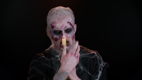 Zombie-Mann-Mit-Make-up-Mit-Falschen-Wunden,-Narben-Und-Weißen-Kontaktlinsen-Zaubert-Zauber-über-Eine-Kerze