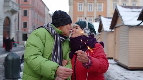Senior-couple-with-burning-sparklers-bengal-lights-celebrating-anniversary,-making-a-kiss-on-street