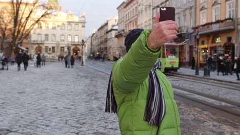 Elderly-tourist-grandfather-traveling,-taking-selfie,-making-online-video-call-on-winter-city-center
