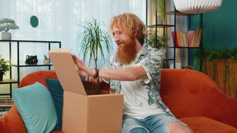 Happy-redhead-man-shopper-unpacking-cardboard-box-delivery-parcel-online-shopping-purchase-at-home
