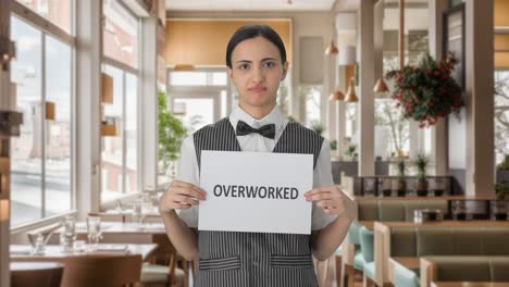 Sad-Indian-woman-waiter-holding-OVERWORKED-banner