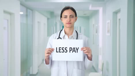Sad-Indian-female-doctor-holding-LESS-PAY-banner