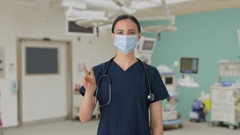 Happy-Indian-female-doctor-showing-victory-sign-with-mask-on