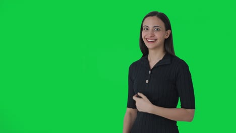 Happy-Indian-female-news-anchor-pointing-at-green-screen-and-showing-okay-sign