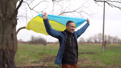 Ukrainian-man.-Young-smiling-man-holding-ukrainian-flag.-No-war.-Support-for-Ukraine.-Patriotic-Spirit-rising-hand-of-Ukraine-flag.-freedom-ukraine.-Nature-background