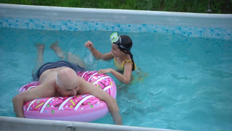 The-grandfather-with-little-granddaughter-have-fun-in-the-pool.-grandfather-plays-with-the-child.-The-family-enjoy-summer-vacation-in-a-swimming-pool-jumping,-spinning,-splash-water.