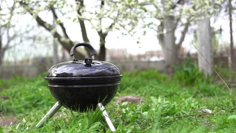 A-metal-barbecue-grill-stands-in-the-backyard-on-the-ground-with-grass-by-the-bushes