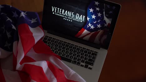 Día-De-Los-Veteranos-Escrito-En-Una-Computadora-Portátil-Con-Bandera-De-Los-Estados-Unidos,-Sobre-Un-Fondo-Rústico-De-Madera