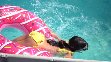 Cute-little-girl-in-a-bathing-suit-lying-on-a-donut-inflatable-circle.-The-child-swims-on-a-blue-background