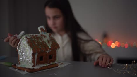 Cute-little-girl-with-gingerbread-spooky-house-with-festive-icing-and-ghost-shaped-cookie.-Happy-Halloween