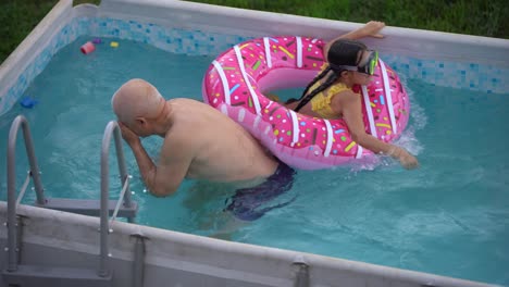 The-grandfather-with-little-granddaughter-have-fun-in-the-pool.-grandfather-plays-with-the-child.-The-family-enjoy-summer-vacation-in-a-swimming-pool-jumping,-spinning,-splash-water.