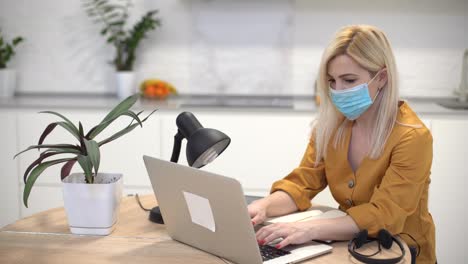 Frau-Mit-Schutzmaske-Arbeitet-Zu-Hause-In-Der-Küche-Ferngesteuert-Am-Laptop