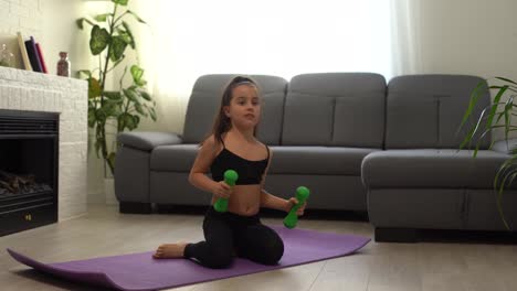 Little-girl-is-doing-squat-exercises-workout-at-home.-Cute-kid-is-training-on-a-mat-indoor.-Little-dark-haired-female-model-in-sportswear-has-exercises-near-the-window-in-her-room