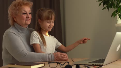 Beginning-of-online-school-classes,-greeting-the-teacher-using-a-video-call.-A-young-grandmother-and-granddaughter-study-on-a-laptop