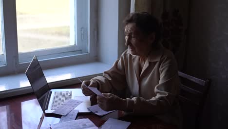 a-very-old-woman-sits-at-a-table-and-checks-bills-for-an-apartment