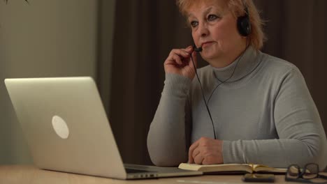 Senior-female-teacher-in-headset-giving-online-lesson-on-laptop
