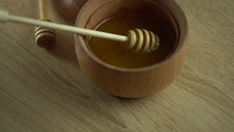 Honey-dripping,-pouring-from-honey-dipper-in-wooden-bowl.-Close-up.-Healthy-organic-Thick-honey-dipping-from-the-wooden-honey-spoon,-closeup.-4K-UHD-video-footage.-Slow-motion