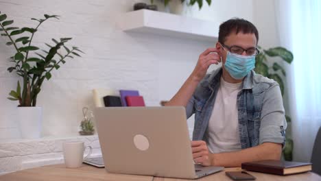man-trying-to-take-off-protective-mask-and-working-on-laptop