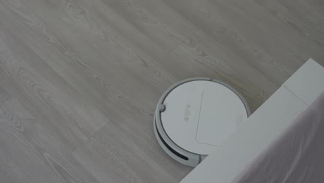 Weißer-Roboterstaubsauger-Auf-Laminatboden,-Der-Staub-Im-Wohnzimmer-Reinigt.-Intelligente-Housekeeping-Technologie.