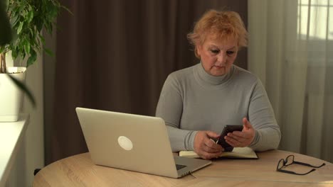 Ancianos-Trabajando-En-Una-Computadora-Portátil-En-Casa.-Retrato-De-Una-Mujer-De-Negocios-Senior-Que-Recibe-Una-Llamada-Telefónica-Y-Trabaja-En-Una-Computadora-De-Forma-Remota-En-Casa
