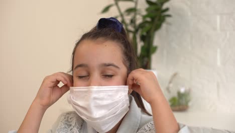 Little-girl-takes-off-her-protective-medical-mask-and-smiles.-Stay-home-mom.-Coronavirus-or-COVID-19.-Cute-little-girl-in-a-protective-mask