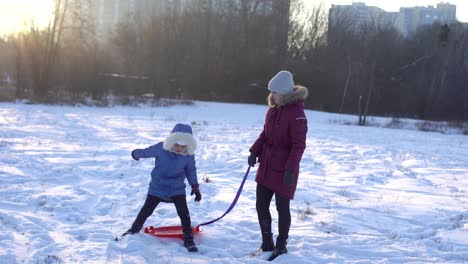 family,-sledding,-season-and-people-concept---happy-mother-pulling-on-ice-sled-with-child-outdoors-in-winter
