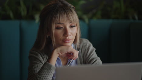 Portrait-of-a-beautiful-young-and-attractive-Asian-woman-is-sitting-and-looks-worried-and-serious-as-she-broods-in-front-of-her-laptop-computer-during-the-day.