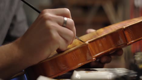 Focused-luthier-varnishing-violin-in-workshop