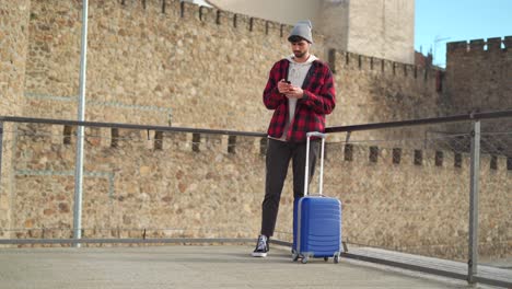 Traveler-with-suitcase-sending-a-message-on-mobile-phone