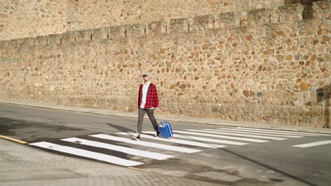 Male-traveler-crossing-a-crosswalk-with-his-luggage