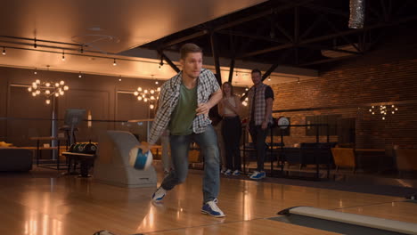 A-man-in-a-bowling-alley-throws-a-ball-on-the-track-and-knocks-out-a-shot-in-slow-motion-and-jumps-and-dances-for-joy.-A-group-of-multi-ethnic-friends-play-bowling-together-clapping-happy-supporting