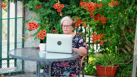 Aged-female-using-laptop-at-table-near-plants