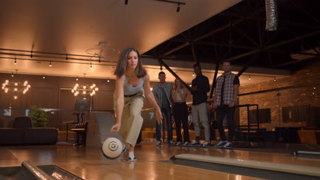 A-woman-in-a-bowling-alley-throws-a-ball-on-the-track-and-knocks-out-a-shot-in-slow-motion-and-jumps-and-dances-for-joy.-A-group-of-multi-ethnic-friends-play-bowling-together.